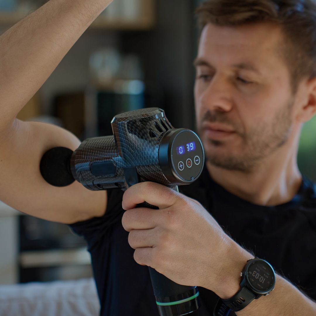 Man using a massage gun on another person's arm in a home setting.