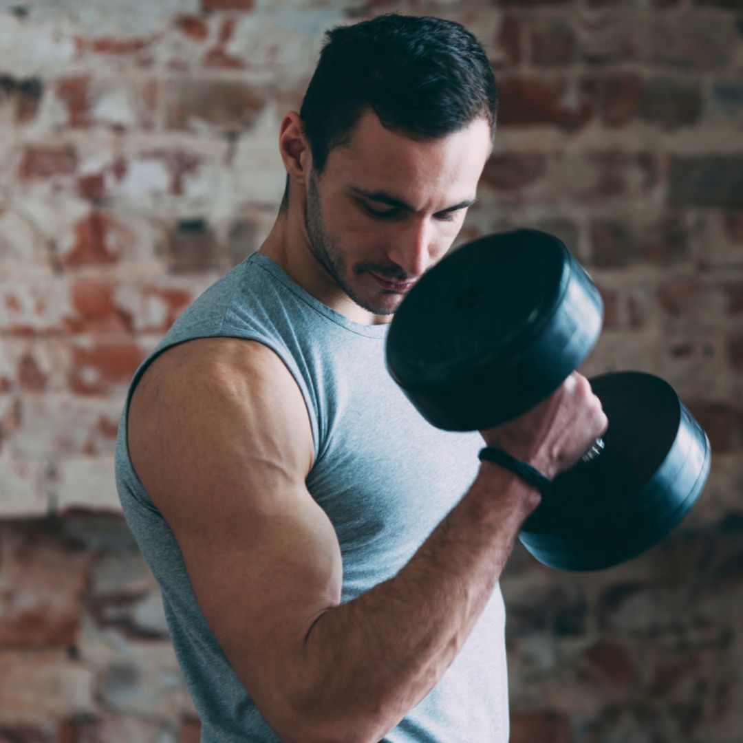 Man lifting a dumbbell in front of a brick wall