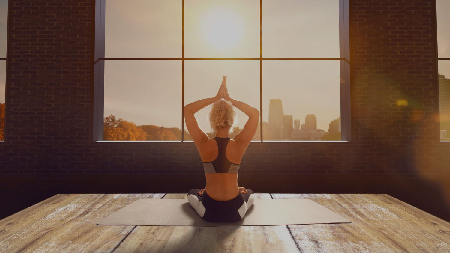 Person practicing yoga in a room with large windows showing a cityscape.