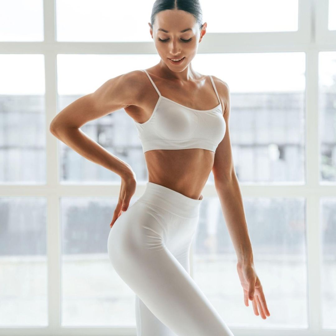 Woman in white athletic wear standing in a bright room with large windows.